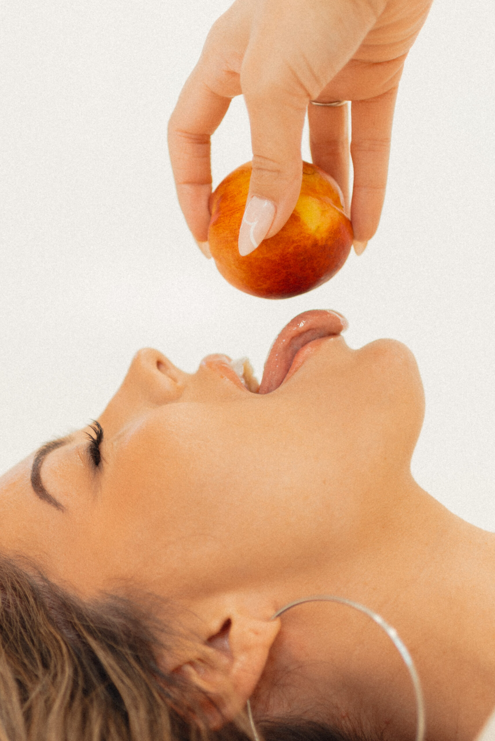 Woman with smooth skin playfully reaching for a peach, symbolizing Brazilian waxing results in Sandy UT
